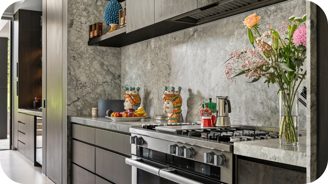 Close-up of a marble kitchen benchtop with a gas cooktop, colourful Sicilian head vases, and fresh flowers adding warmth to the design.