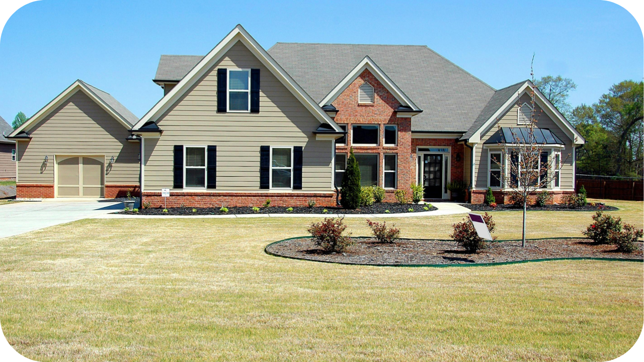 Large suburban brick and beige house with gabled roofs, wide driveway, and front garden under clear blue sky.