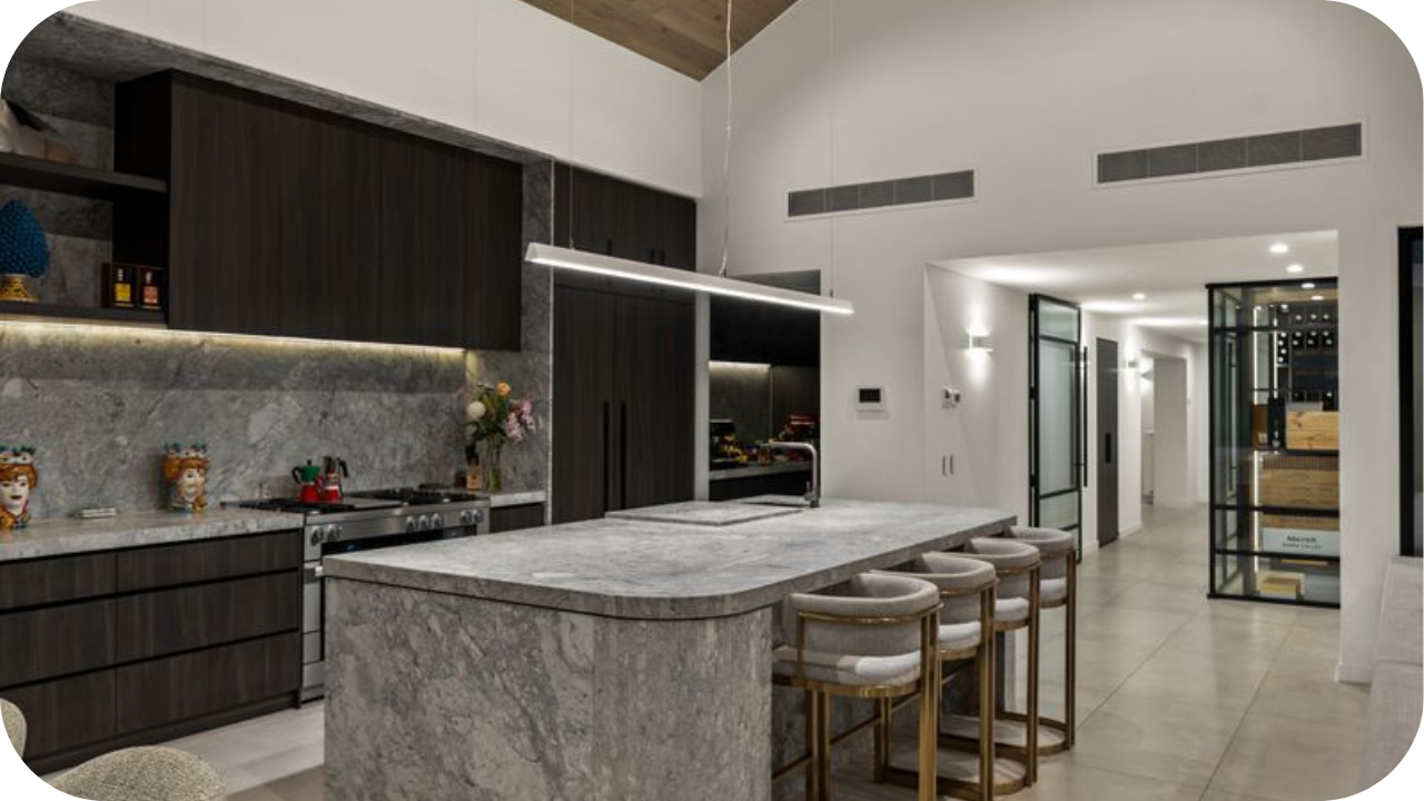 Modern kitchen with stone benchtops, dark cabinetry, pendant lighting, and soft grey finishes reflecting material and design trends in Queensland and Victoria.