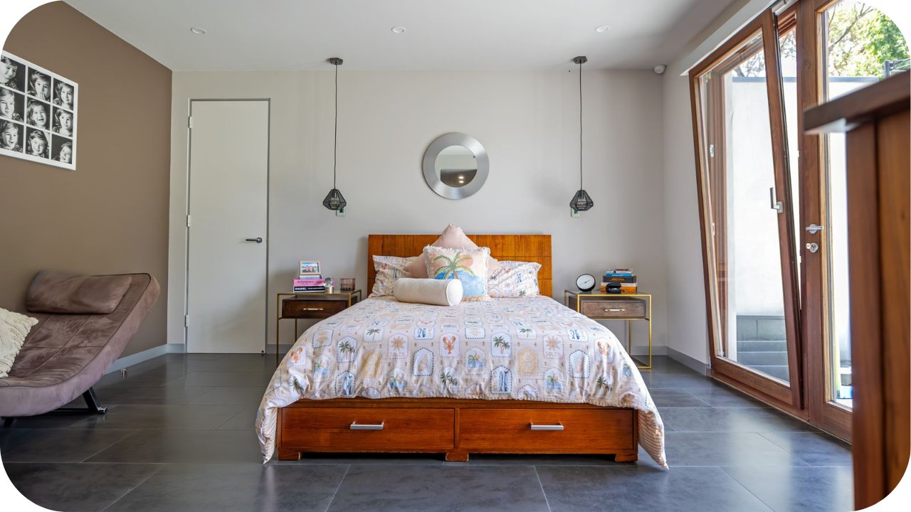 A bright luxury bedroom with timber bed frame, pendant lights, large glass doors, and warm neutral styling, reflecting modern interior trends in Melbourne and Brisbane homes.