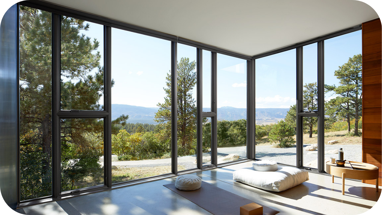 Serene wellness space with floor-to-ceiling windows, natural light, minimalist cushions, and panoramic views of trees and distant mountains for a luxury home feature.