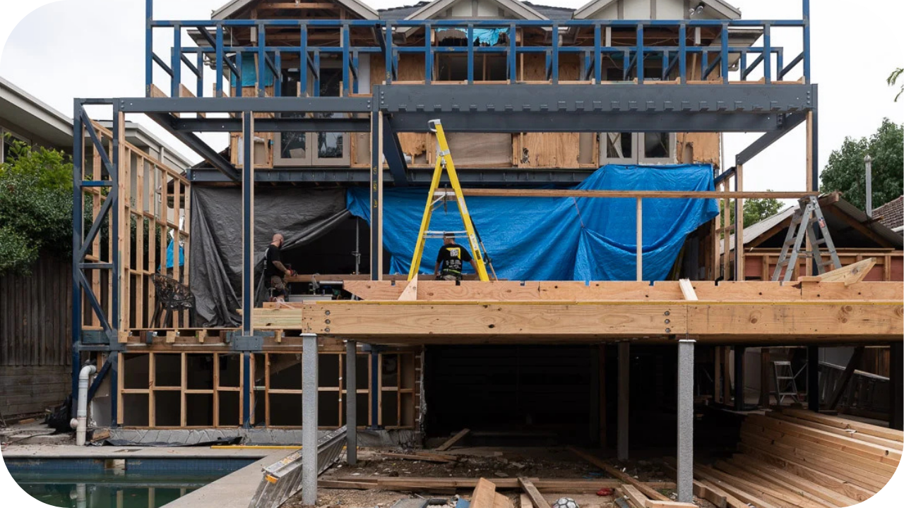 Builders working on a large Melbourne home extension with exposed framing, structural supports, and active construction showing key stages of planning and build preparation.