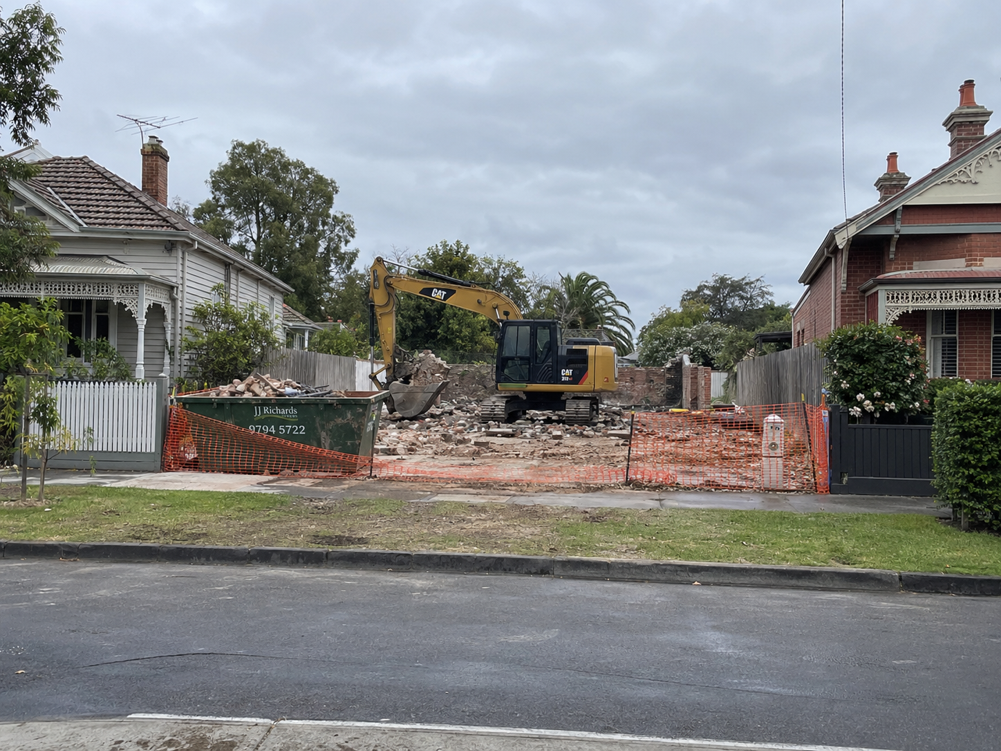 Excavator clearing a demolition site between two intact period homes
