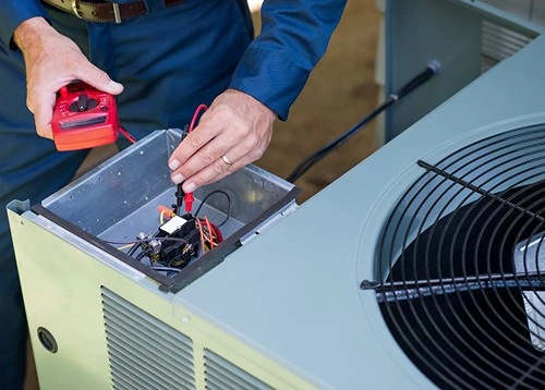 Technician using multimeter to test electrical components in HVAC unit