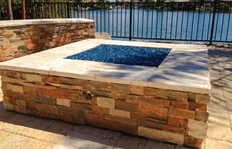 Stone fire pit with blue glass stones near waterfront railing