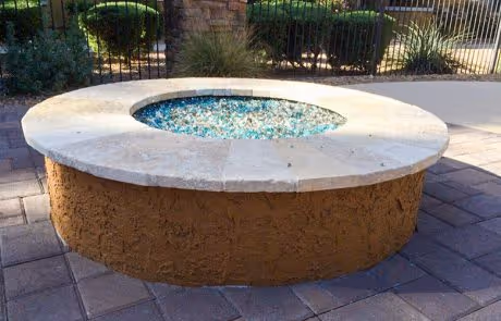Round stone fire pit with blue glass stones on paved outdoor patio