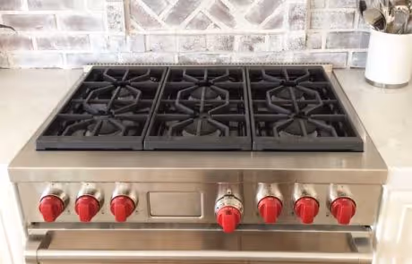 Stainless steel gas cooktop with six burners and red control knobs