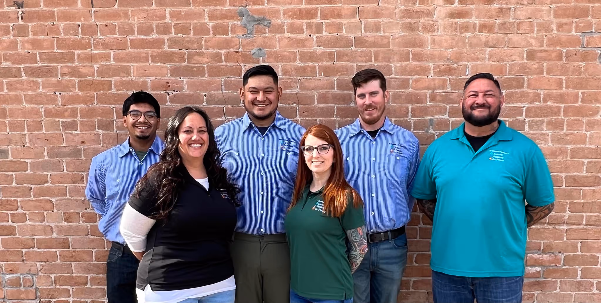 Six smiling team members posing in front of brick wall