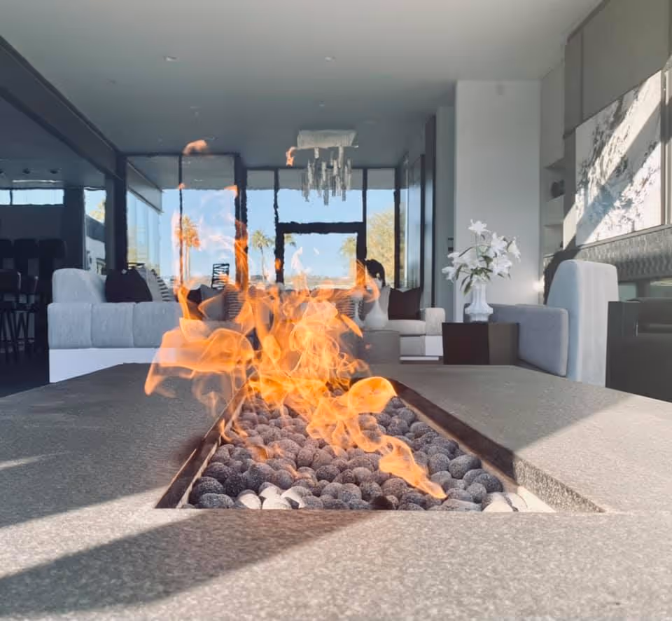 Modern living room with blazing fire pit and glass walls overlooking trees