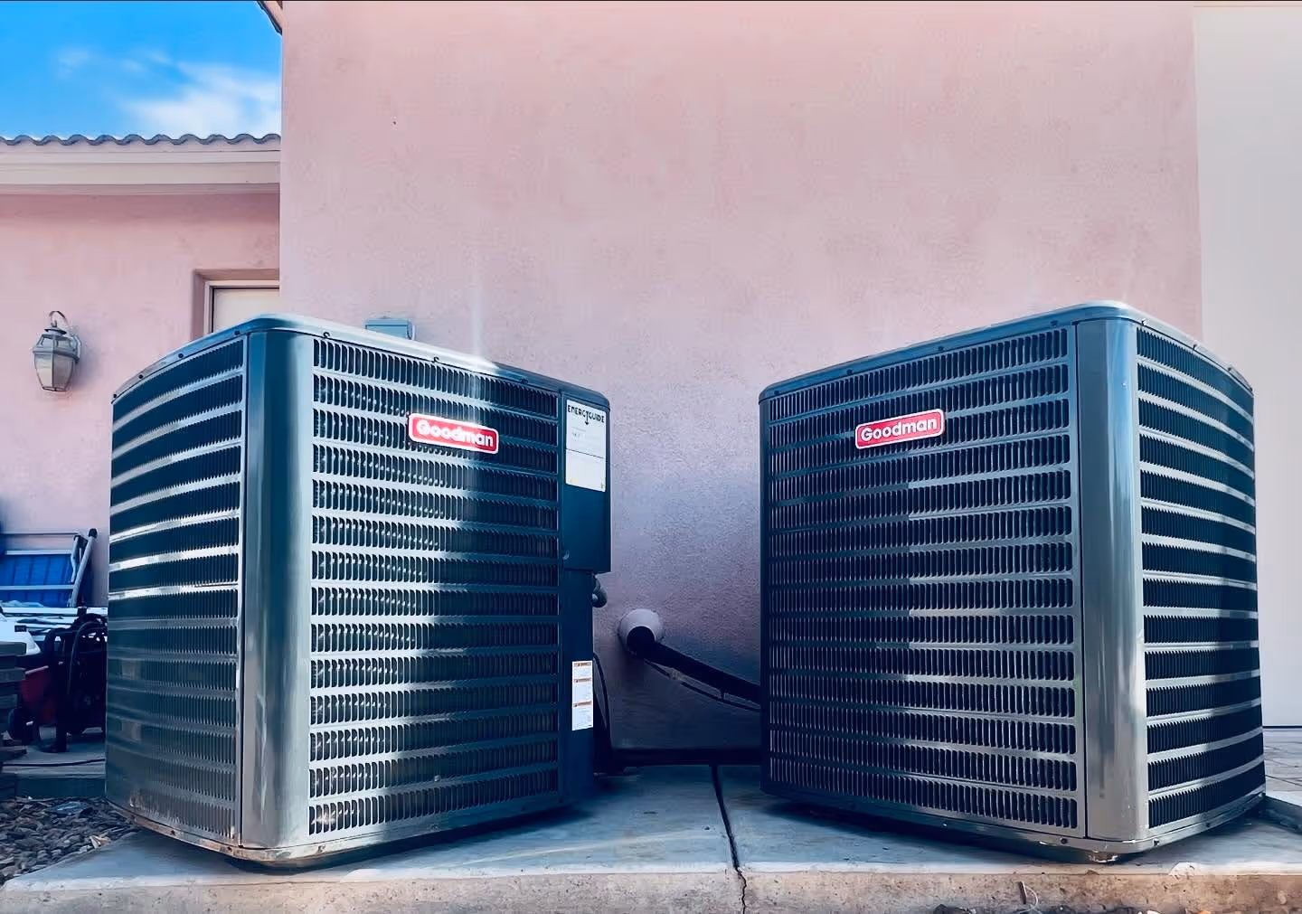 Two Goodman air conditioning units installed outside a pink building