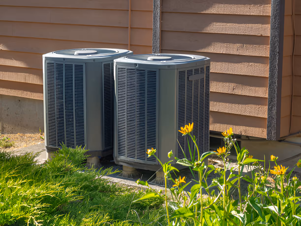 Two air conditioning units near yellow flowers and green grass