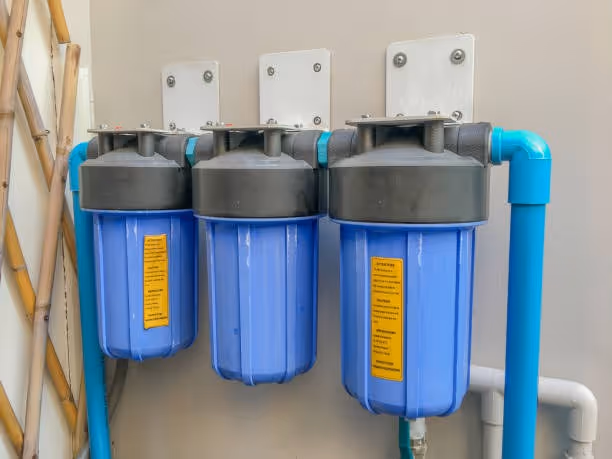 Three blue water filtration systems mounted on wall with blue and white pipes