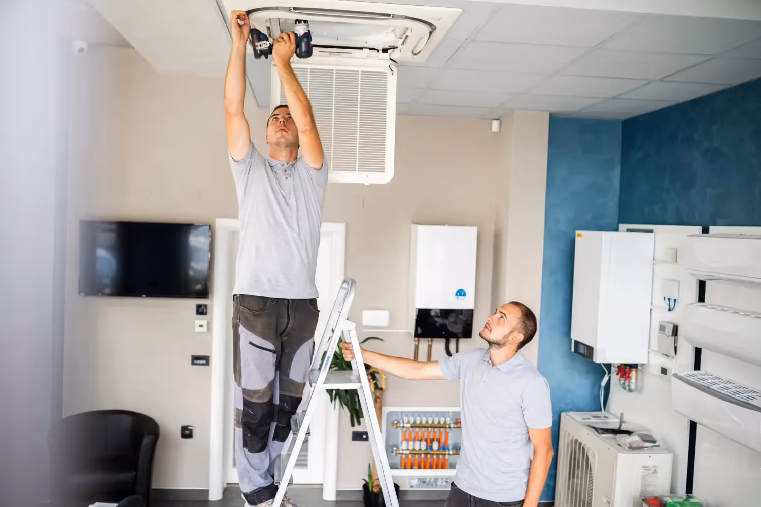 Two technicians installing or repairing a ceiling air conditioning unit