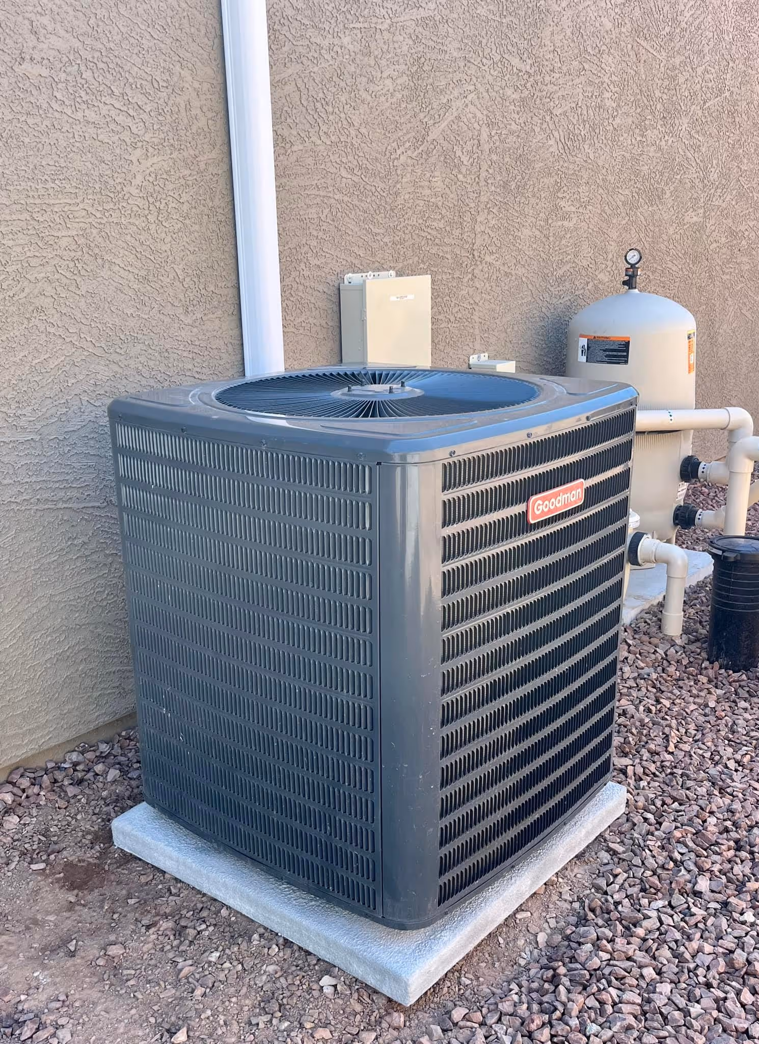 Goodman air conditioning unit on concrete pad next to stucco wall