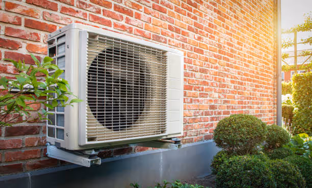 Air conditioning unit mounted on brick wall with green plants nearby