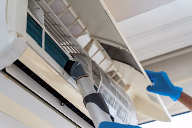 Person cleaning air conditioning unit with vacuum and gloved hand