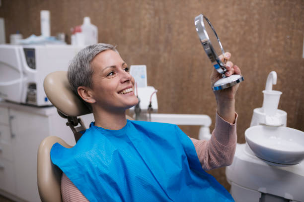 Happy mid adult woman in a dental chair looking into mirror in clinic Happy mid adult woman in a dental chair and looking in the mirror. Female patient looking at the result of treatment into the mirror and smiling at dental clinic. patient holding smile at dentist stock pictures, royalty-free photos & images