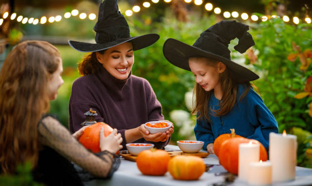 family preparing for Halloween Happy family preparing for Halloween. Mother and children carving pumpkins in the backyard of the house. family halloween party stock pictures, royalty-free photos & images