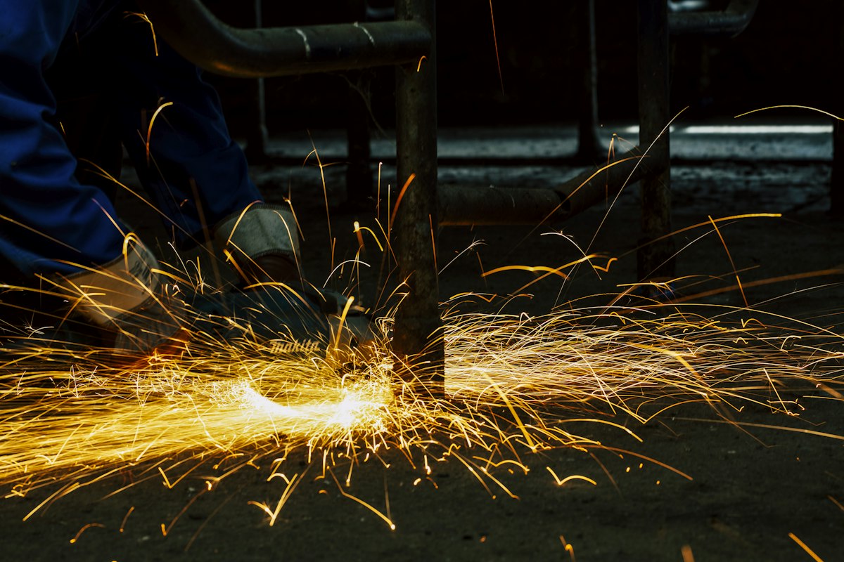 A welder joining metal with visible sparks in a fabrication shop
