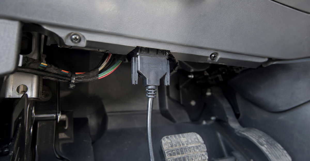 ELD diagnostic cable connected to a commercial truck engine control module port under the dashboard