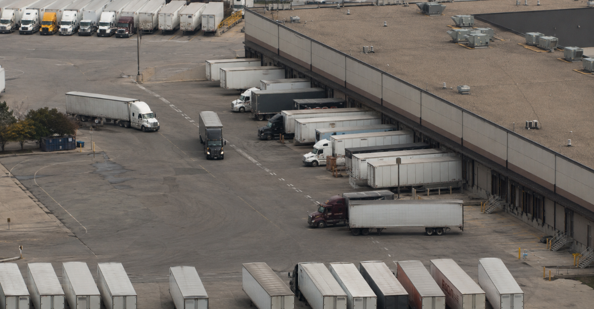 Aerial view of a distribution terminal with trucks loading at dock doors and trailers staged across the yard