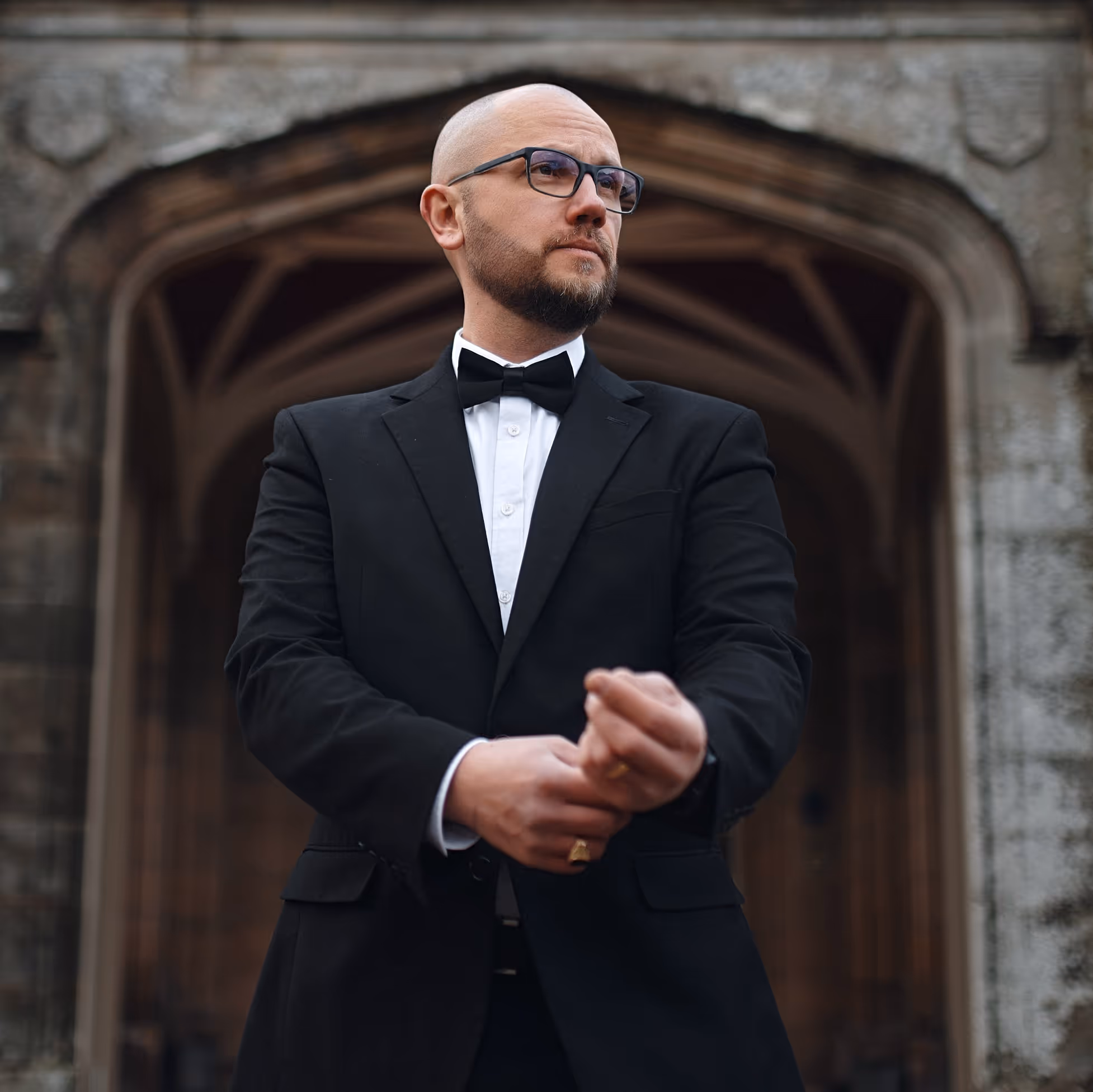 A bald man wearing a black suit and a bow tie.