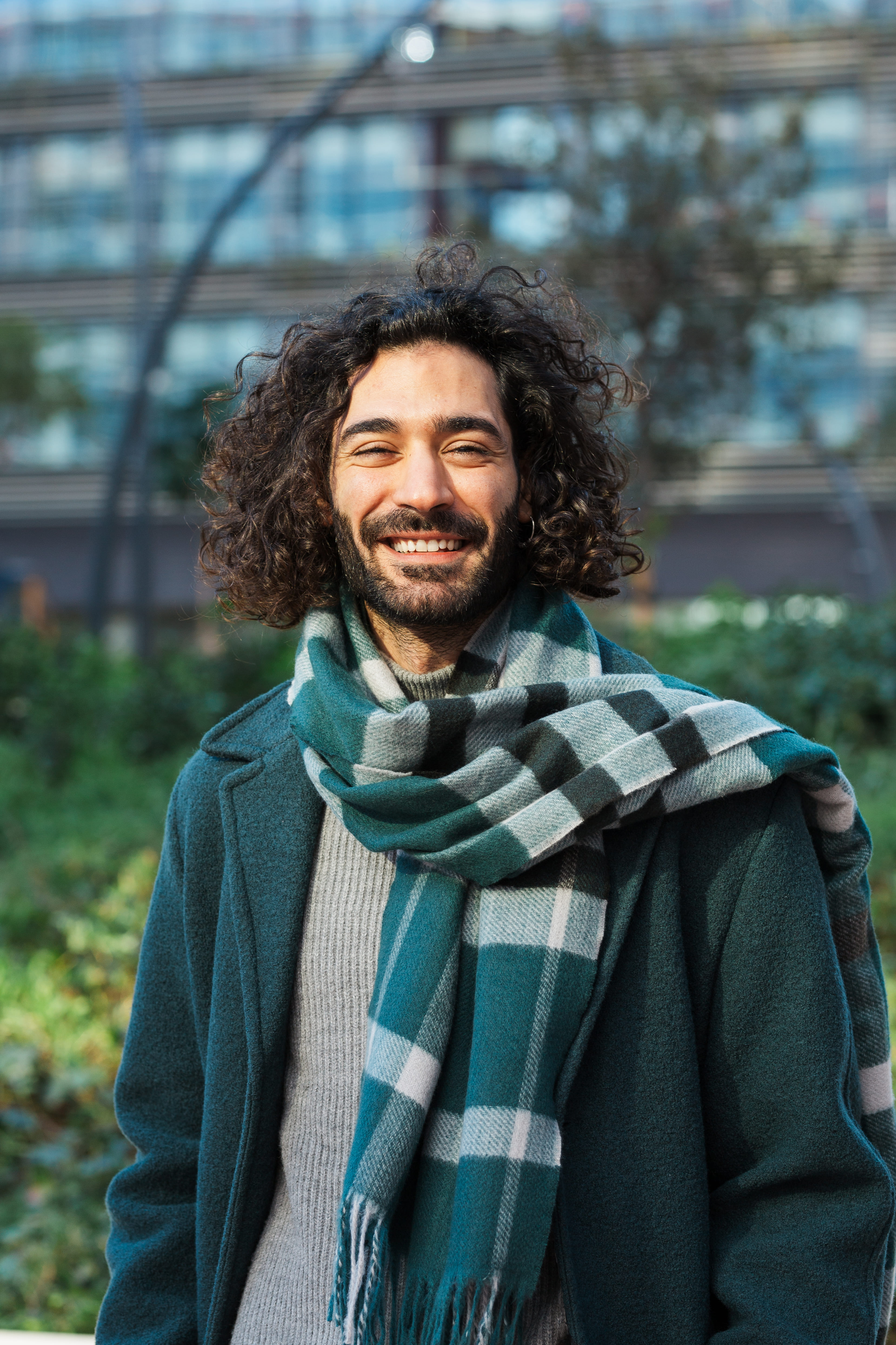 A man with a green scarf and curly hair smiles for the camera.
