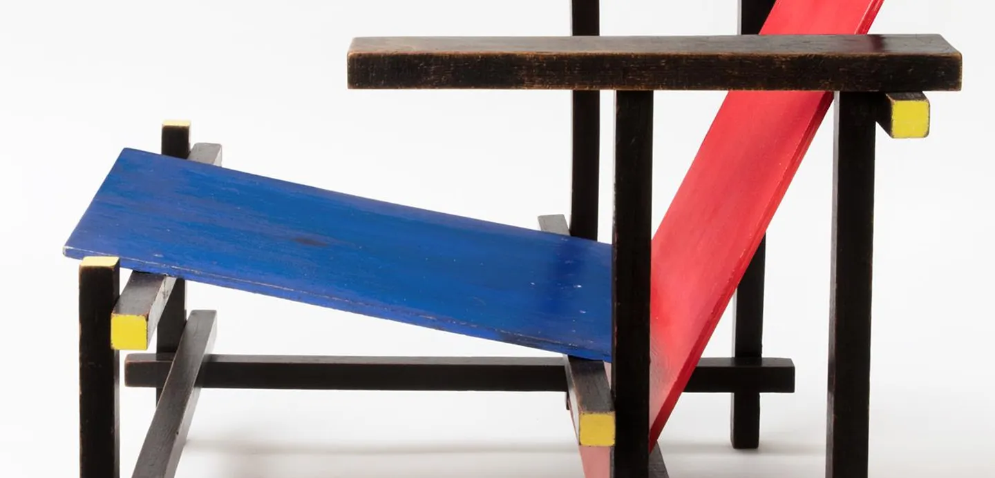 Detail stoel, deel van een blauwe zitting, rode rugleuning, en zwarte latten met gele kanten