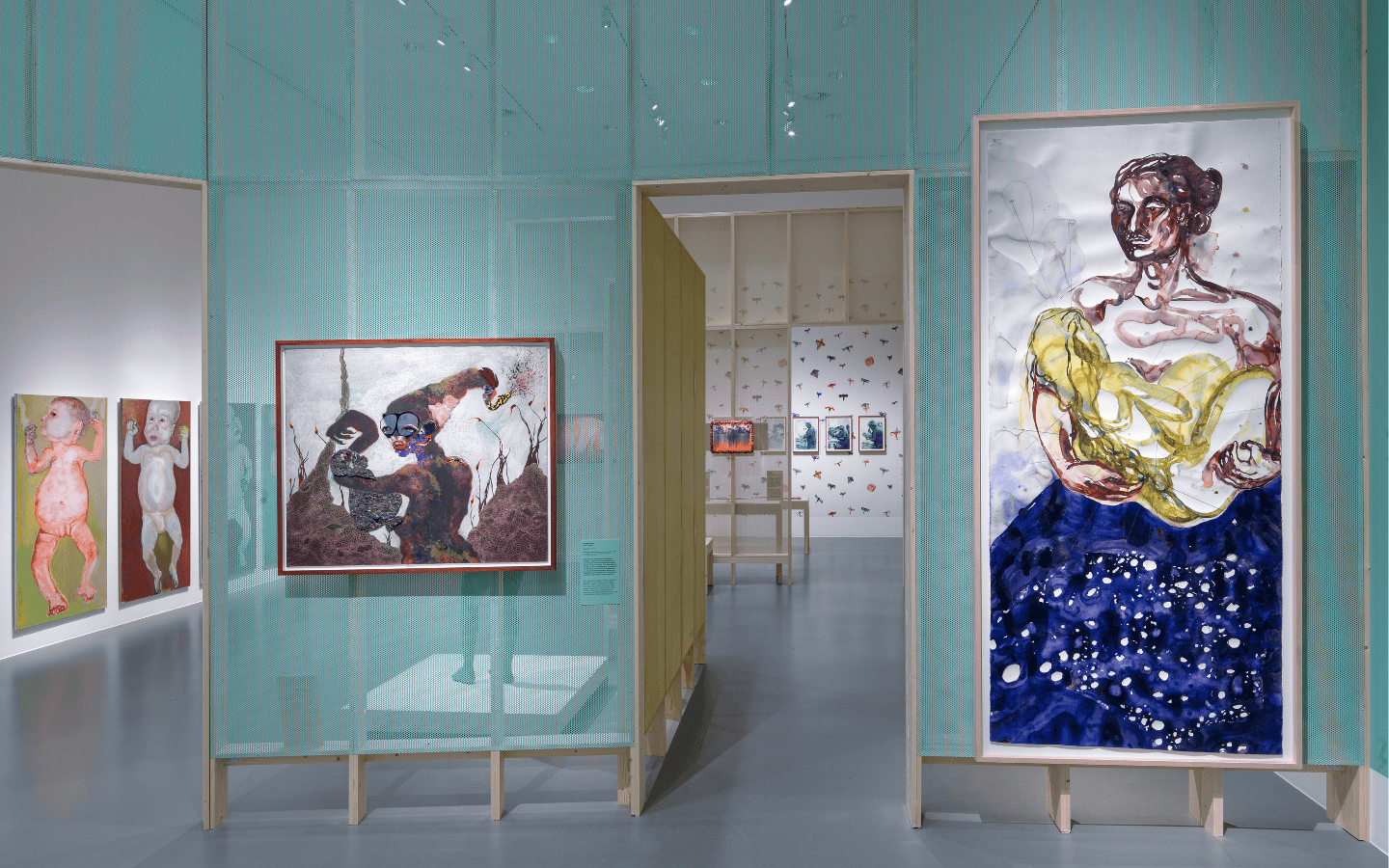 Een grijsblauwe museummuur met verschillende kunstwerken. Links zie je twee babies. Rechts een vrouw met blauwe jurk