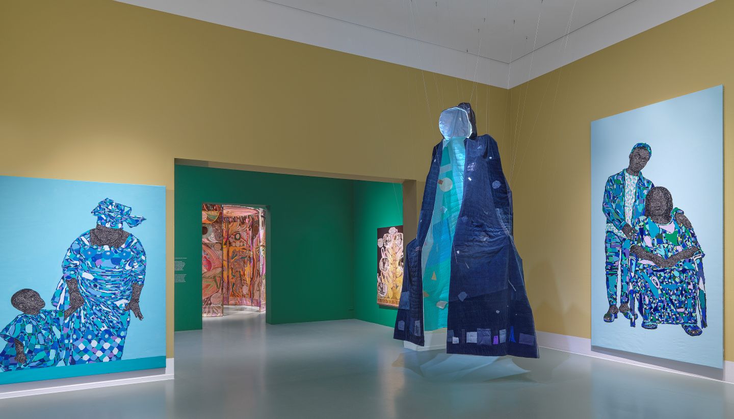 Een gele museummuur met verschillende kunstwerken en een kunstinstallatie in de museumzaal
