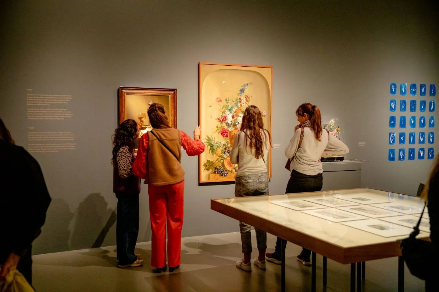 Bezoekers in de tentoonstelling Getekend, de Natuur met op de voorgrond een tafel met tekeningen en op de achtergrond een werk met bloemen en exotisch fruit.