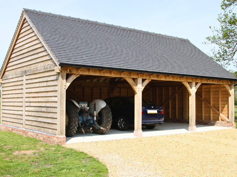 Three-bay open-fronted wooden carport with a car and a tractor parked inside.