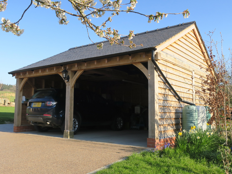 Walton two-bay garage with a black SUV parked inside, surrounded by green lawn and flowering trees under a clear blue sky.