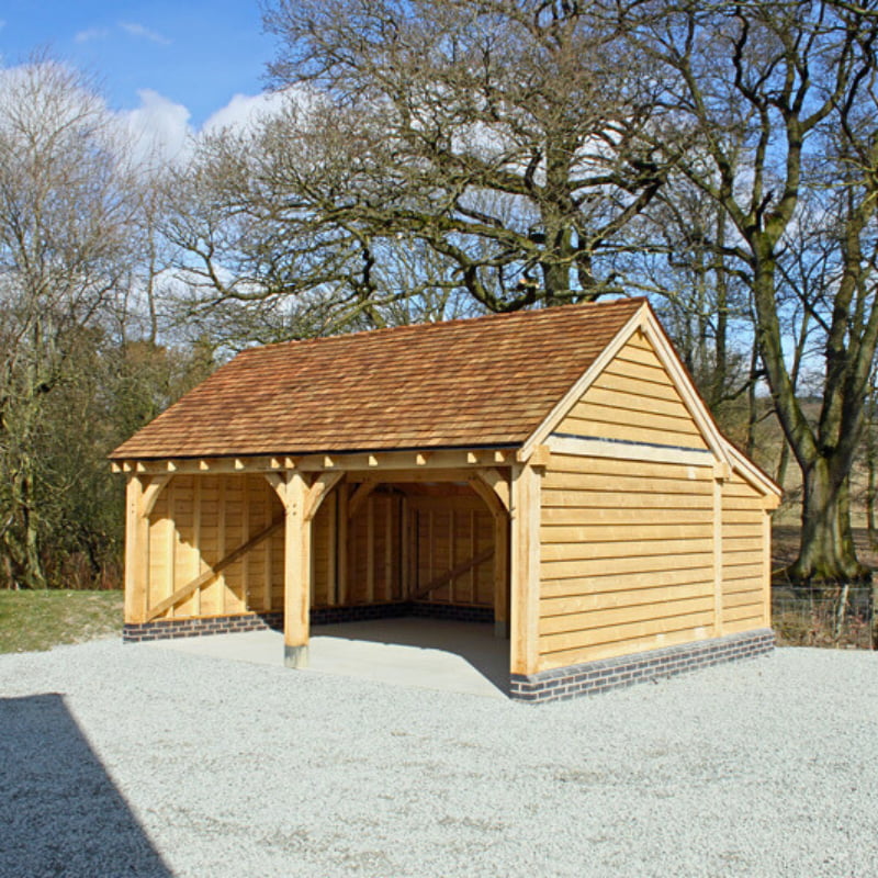 A wooden two-bay garage surrounded by woodland and leading to an open driveway