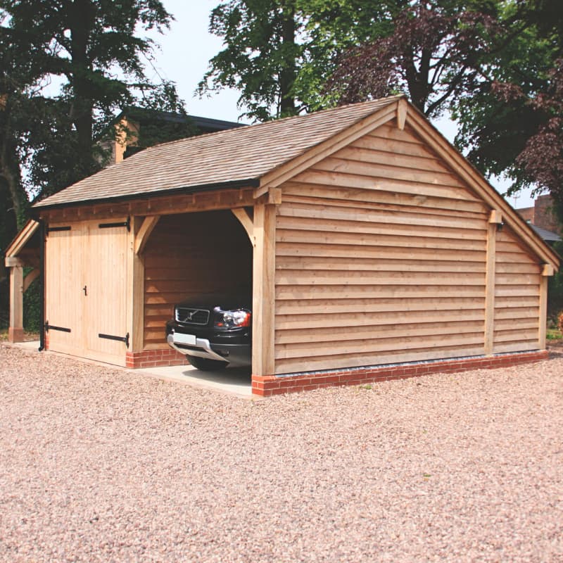Single-storey oak-framed garage with a slate roof, one bay for open carport and one bay for enclosed room with garage doors.