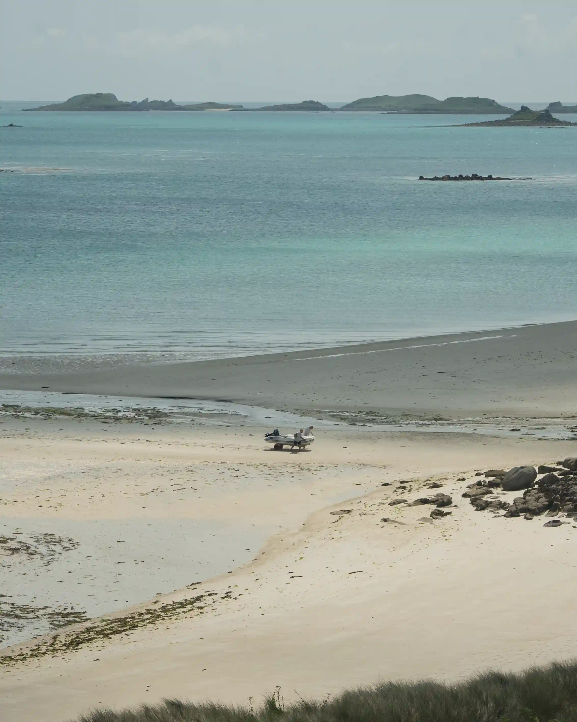 A boat in the distant beach being moved by 2 people
