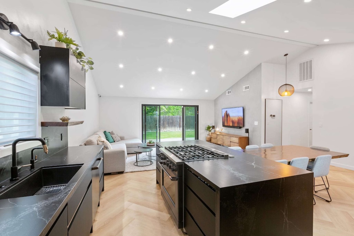 Contemporary open-plan kitchen and living room with black cabinetry, island cooktop, and recessed ceiling lights