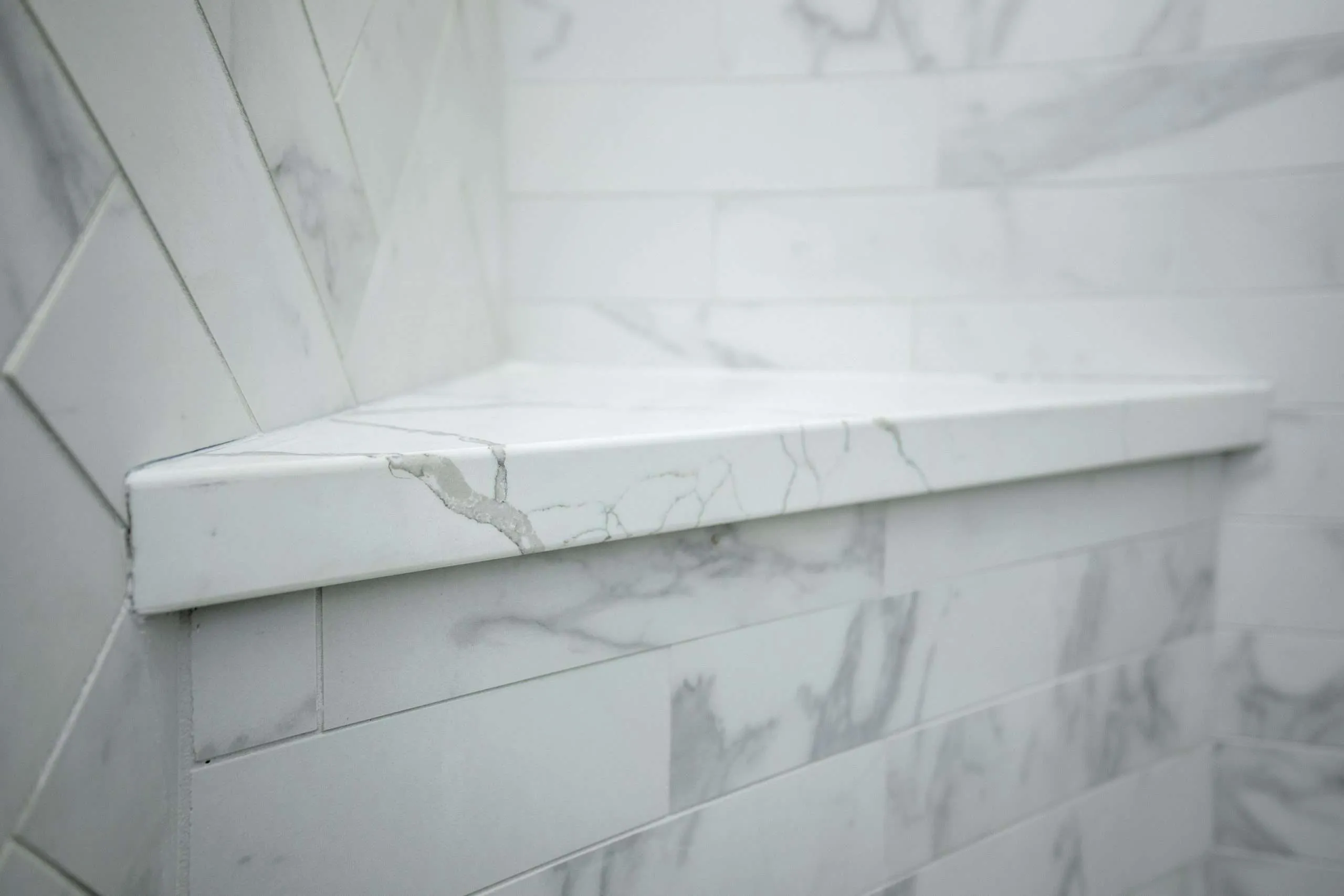 Close-up of a marble shower shelf with surrounding white and gray tile in a bathroom