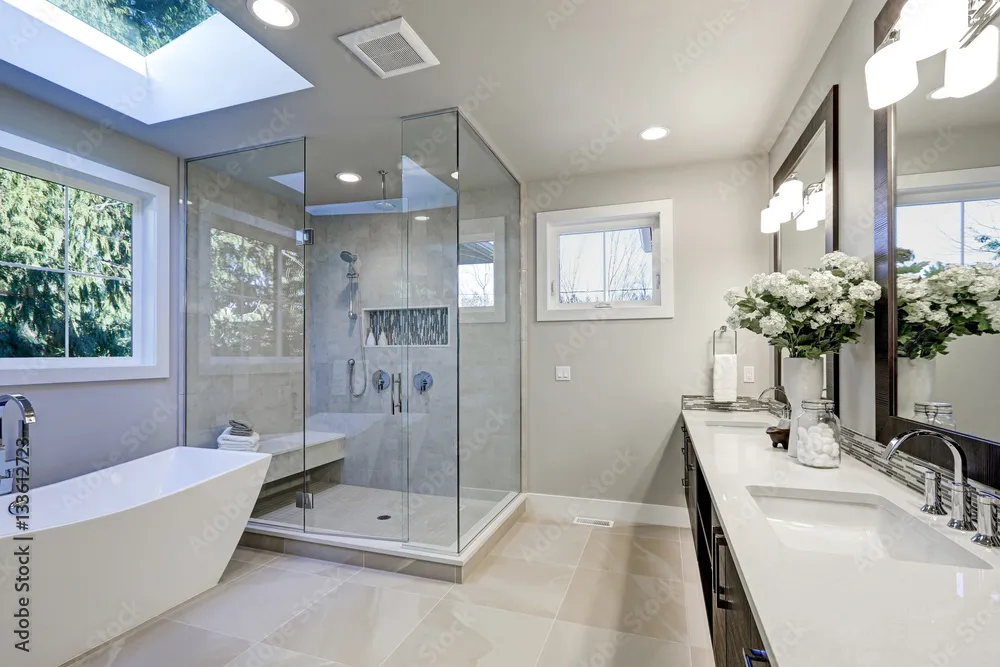 Modern bathroom with freestanding bathtub, large glass shower enclosure, double sink vanity, skylight, and large windows providing natural light.