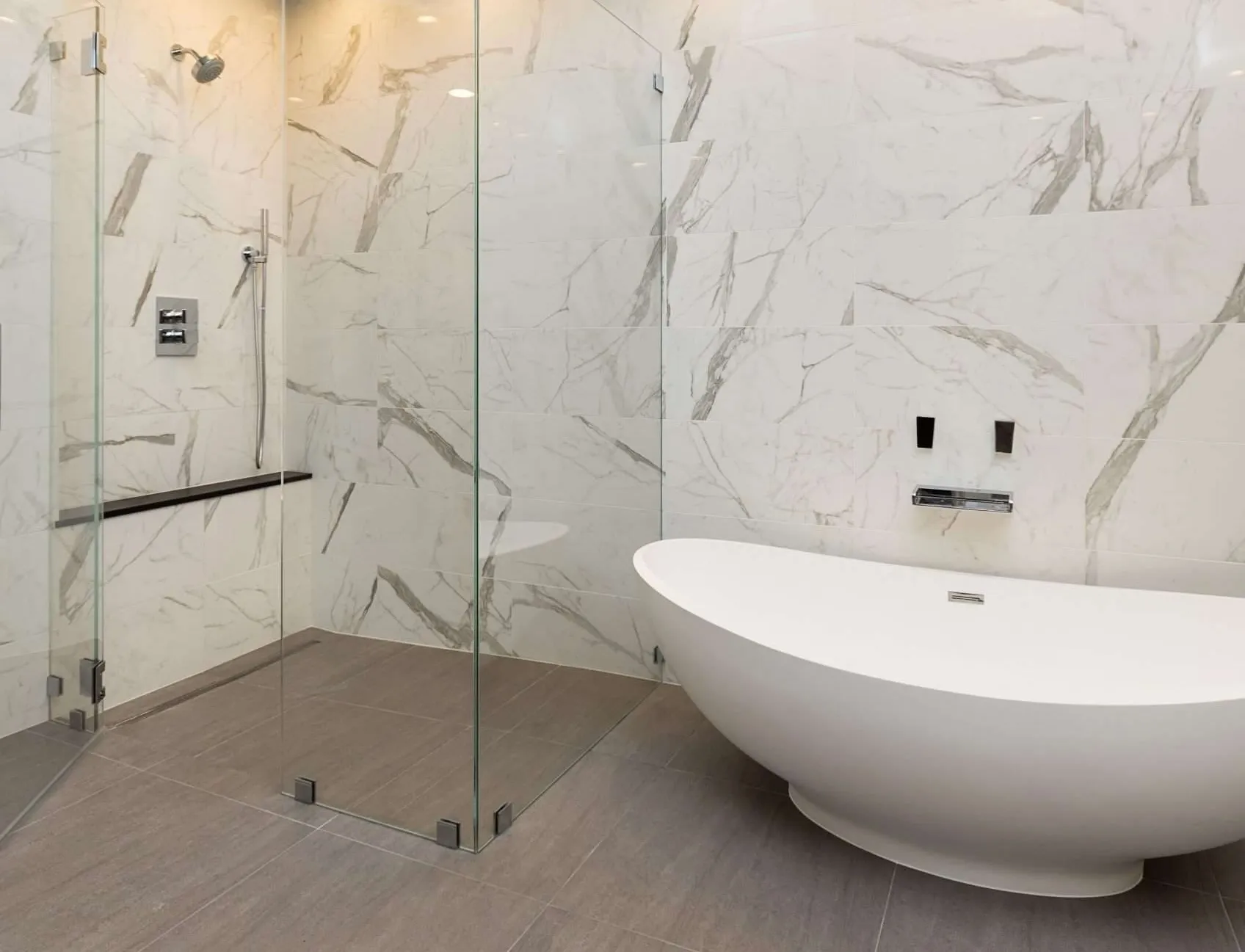 Minimalist bathroom featuring a standalone oval bathtub, large marble tiles, and a glass-enclosed shower area