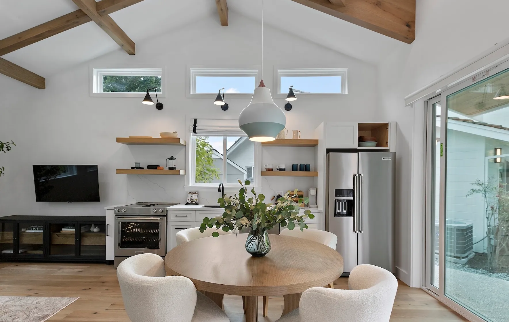 Modern kitchen with vaulted ceiling, wood beams, open shelving, and round dining table