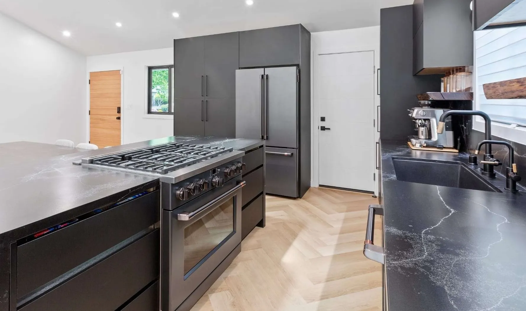 Close-up view of a contemporary black kitchen with a large gas stove, refrigerator, and espresso machine