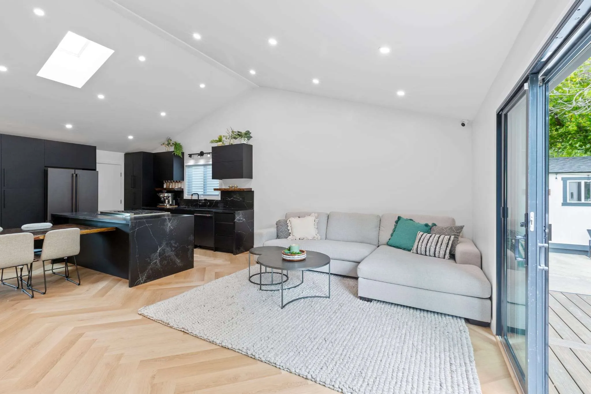 Modern open-concept living room and kitchen with black cabinetry, wood flooring in a herringbone pattern, and a large sectional sofa