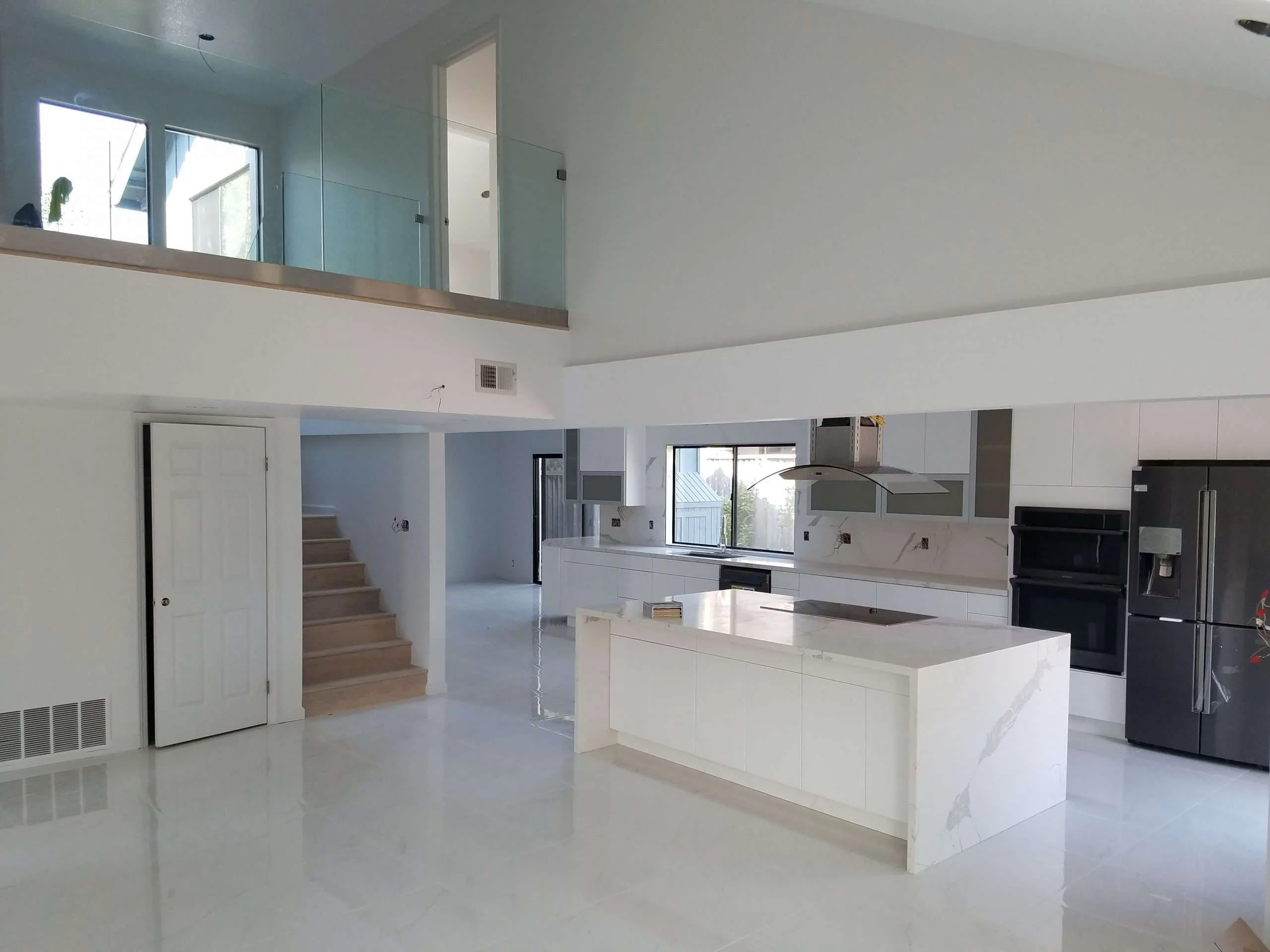 Modern open-concept kitchen with white cabinetry, marble island, and stainless steel appliances in a two-story home with glass railing loft
