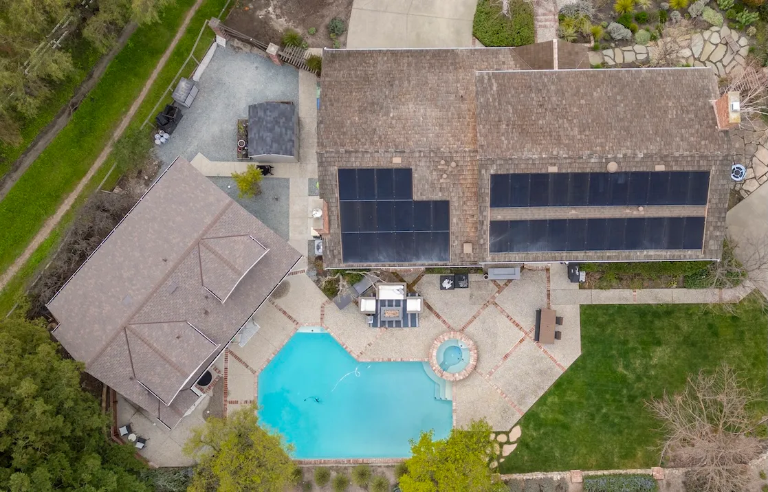Aerial view of a home with solar panels on the roof, a swimming pool, hot tub, and landscaped backyard area
