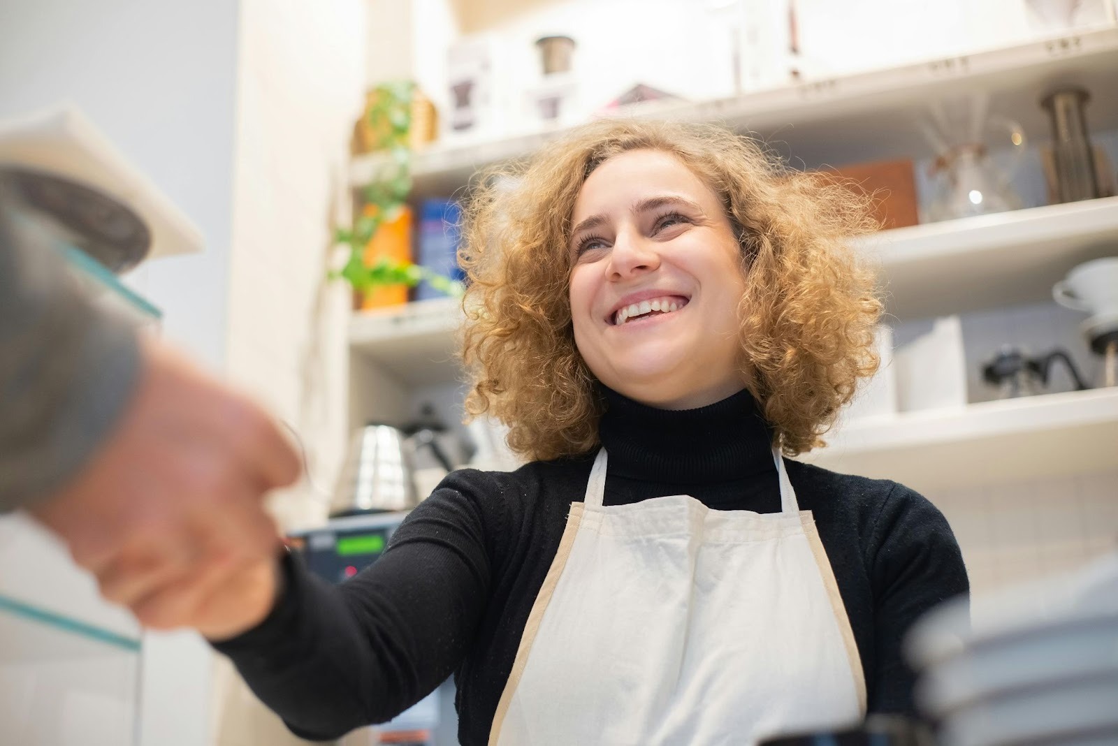 An employee wearing an apron shaking hands with a customer.