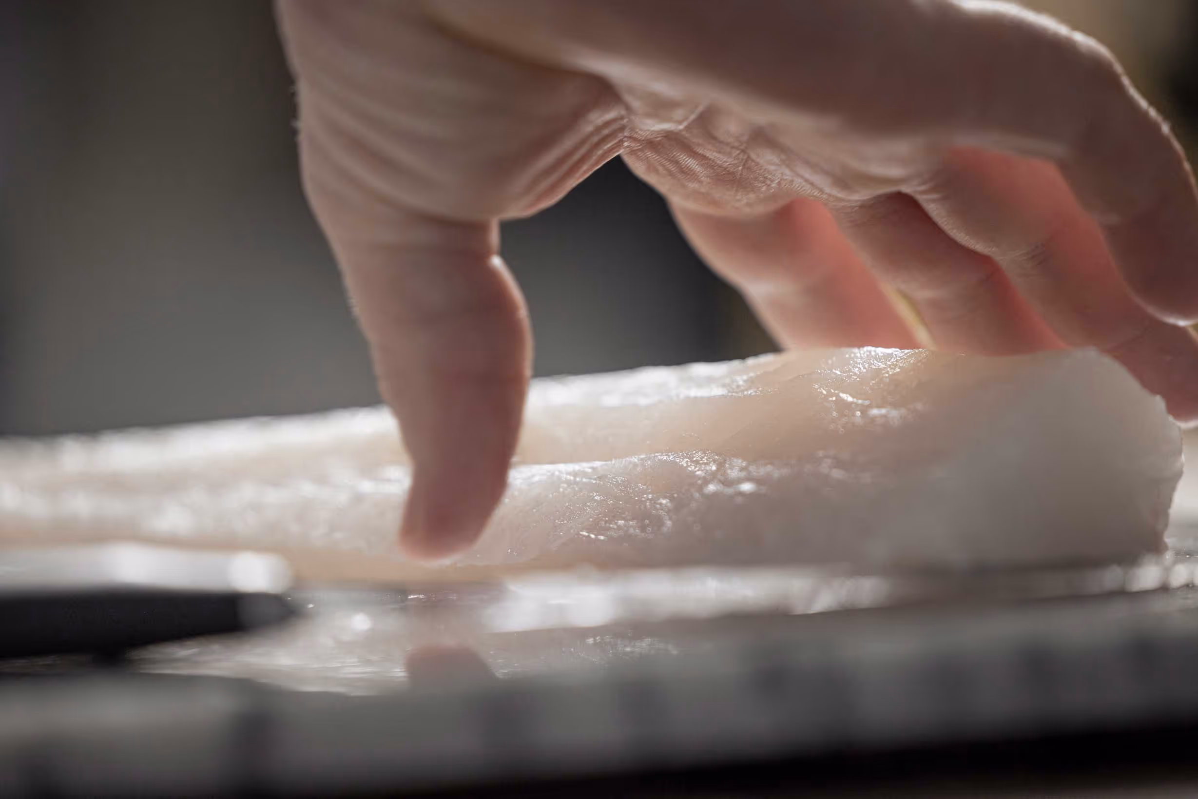 Hand touching white fish on a stone cutting board