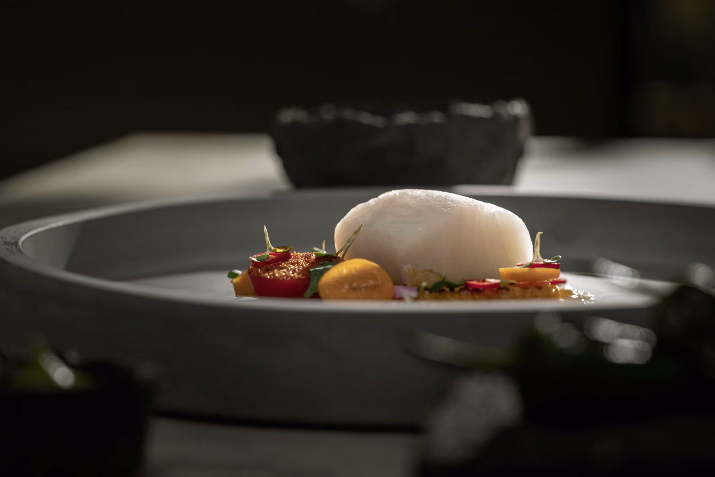 Plated white fish with colorful garnishes on a gray ceramic dish.