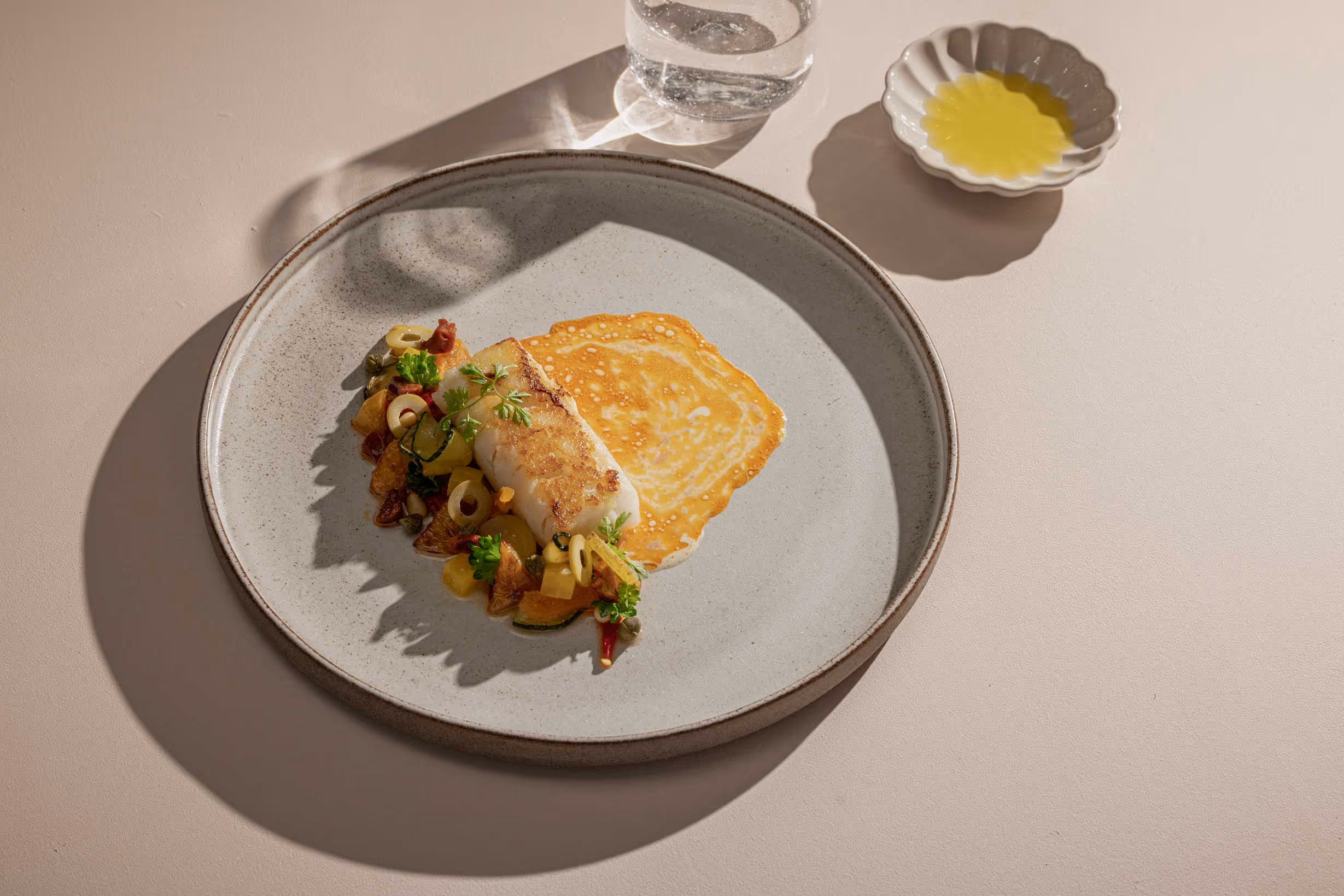 Plated cod with colorful garnishes on a gray ceramic dish.