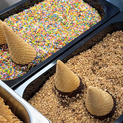 Blick auf bunte Streusel und goldenen Krokant mit frischen Eistüten